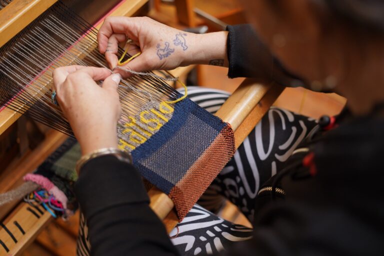 A participant weaves the word "Haystack" on a loom. Photo by Dan Rajter. Image courtesy of Haystack Mountain School of Crafts.
