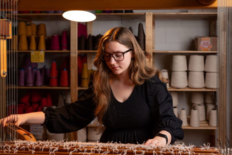 Student Gabbi '27 weaving tea towels that she designed to honor both her family and the College's 4th Great Commitment to the Dignity of All Labor. Sean Hall '25 and Evy Medley '25