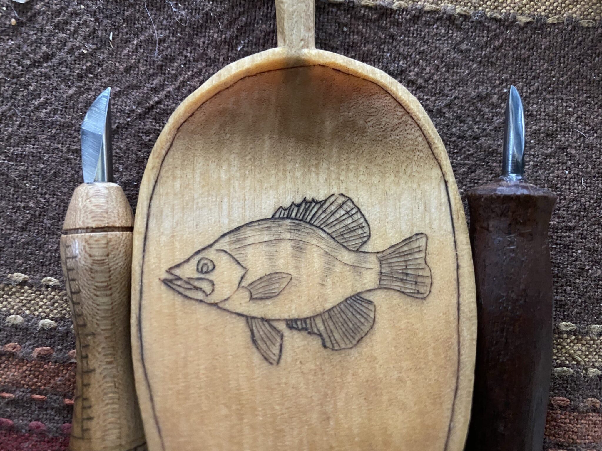 Kolrosed fish image on a wooden spoon with carving knives for kolroshing. American Swedish Institute