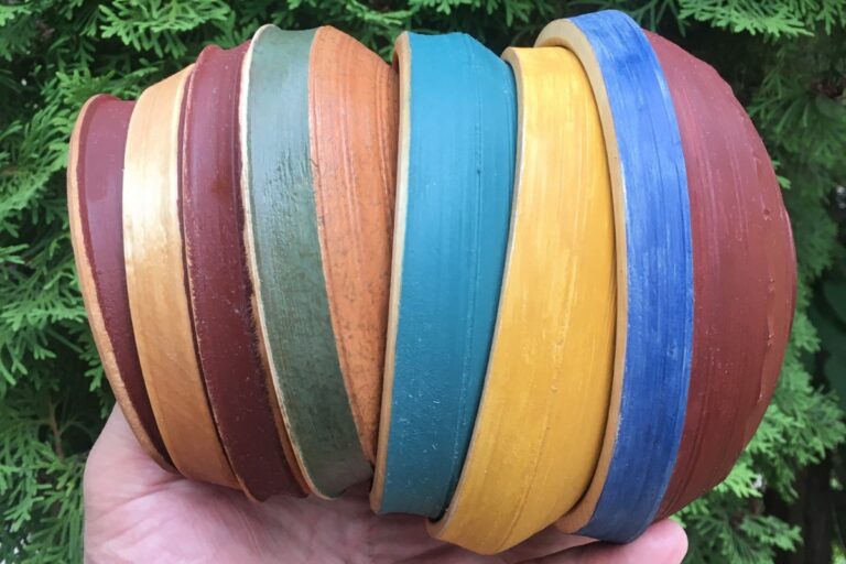 A hand holds a stack of brightly colored, wooden bowls. American Swedish Institute