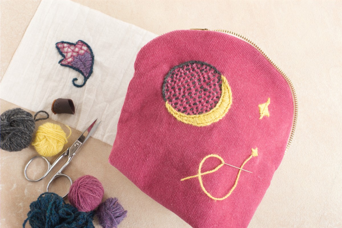pink zippered pouch adorned with celestial embroidery, surrounded by various crafting supplies like yarn and scissors. American Swedish Institute