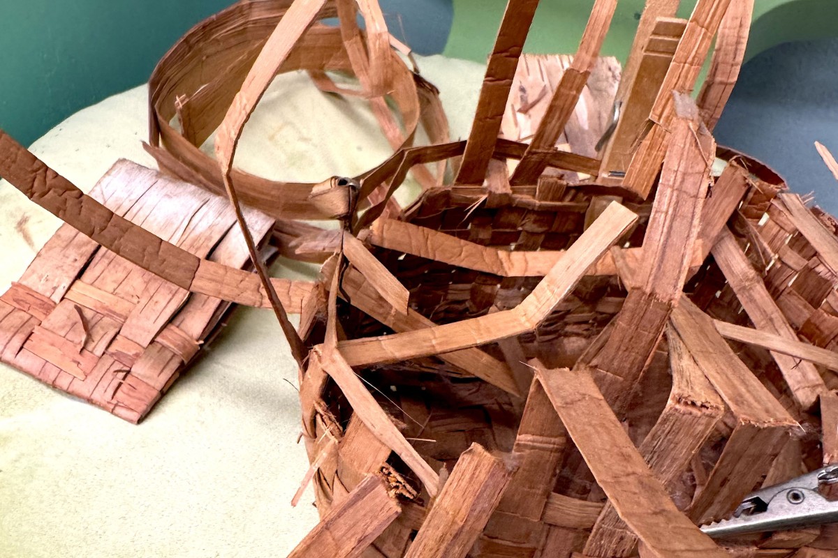 A partially completed birch bark basket made of thin strips of bark woven together. American Swedish Institute