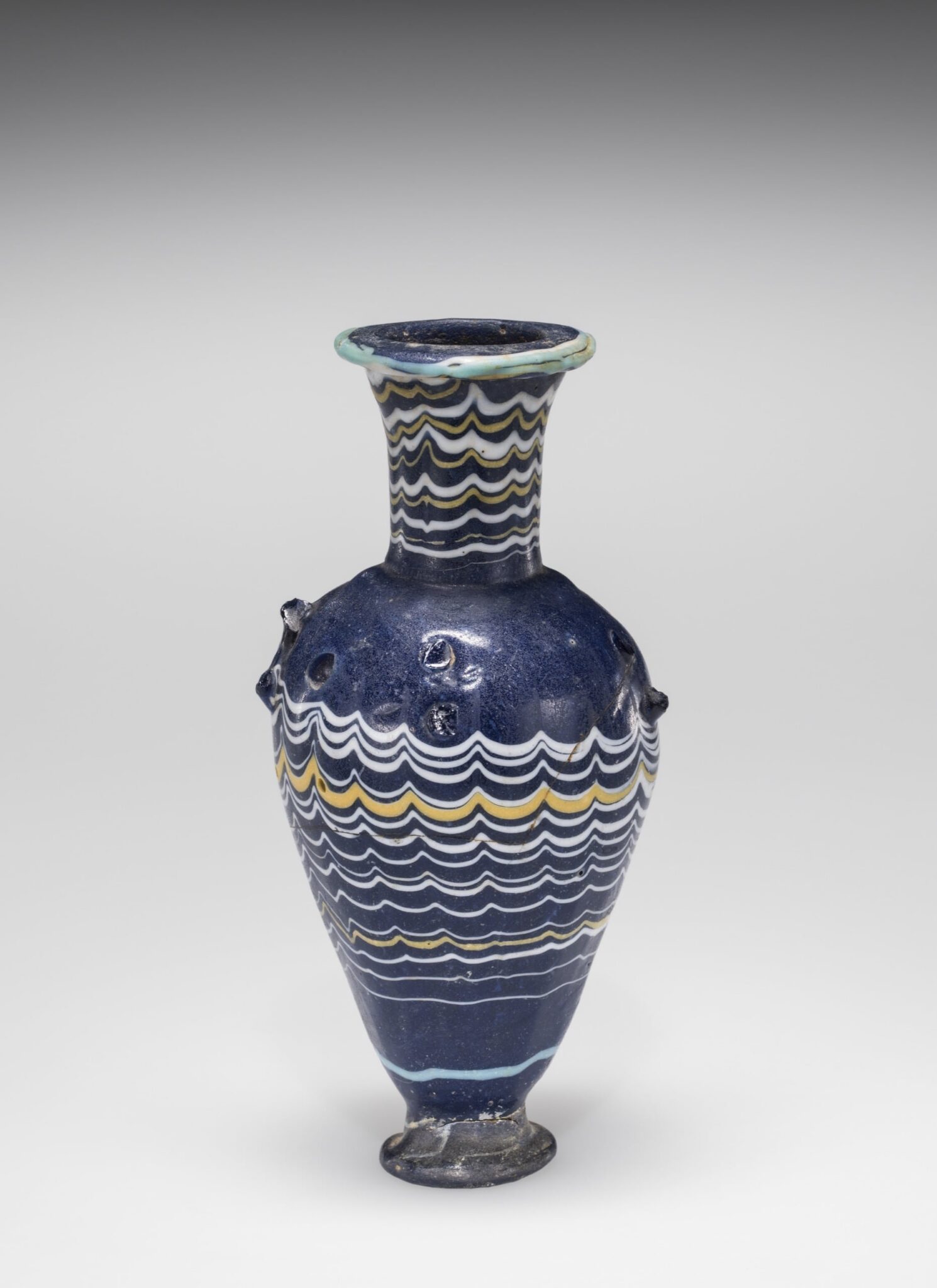 Amphoriskos (Cosmetic bottle). Made in Egypt, probably sometime between 1400 BCE and 1300 BCE. Core-formed glass, trail decorated and hot worked. 50.1.1. Image courtesy of the Corning Museum of Glass.
